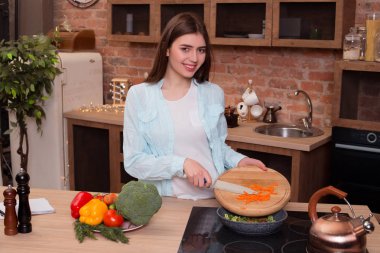 Yeşil olması. Sebzeler yemek! İyi bir akıllı gülümseyen kız verdurous Yeşiller onu sağlıklı ve lezzetli akşam yemeği için havuç doğrama süre onun çağdaş mutfak kamera için poz uygun.