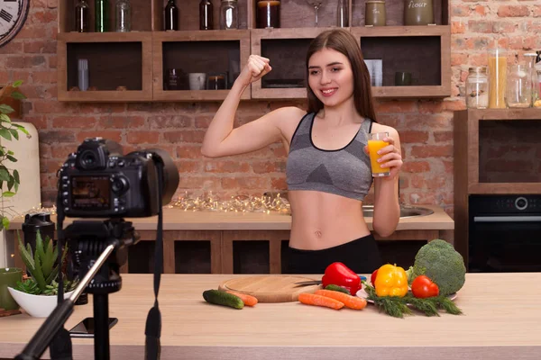 Comprométete a estar en forma! Joven chica atractiva mientras está en la cocina y beber un jugo de naranja, mostrando su cuerpo fuerte y en forma para todos para la cámara . — Foto de Stock
