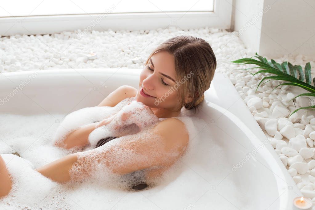 Revitalize your beauty! Gorgeous good-looking young woman relaxing in bath with bath foam with serene smile and closed eyes.