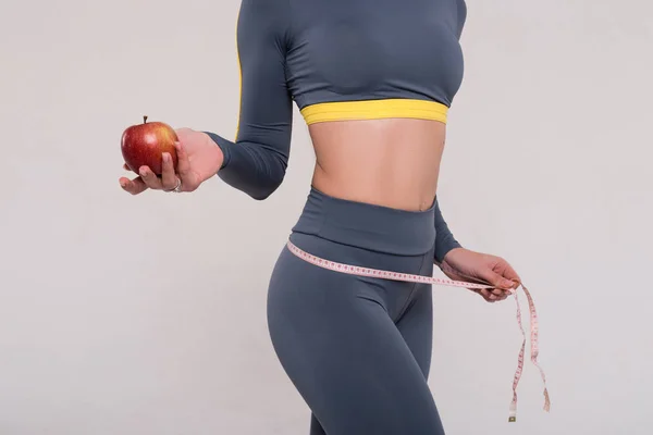 The human body is the best work of art. Closeup picture of the young slim fit girls body with a red apple in the hand and a measure tape on the pelvis. — Stock Photo, Image