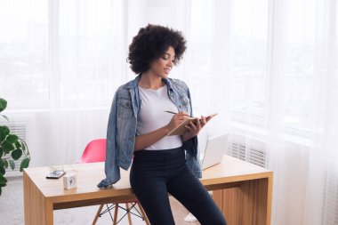 Büyük bir zevk ile iş! Genç yakışıklı zeki kız notları, çalışma masasına kenarında oturan ve gülümseyen yapma.