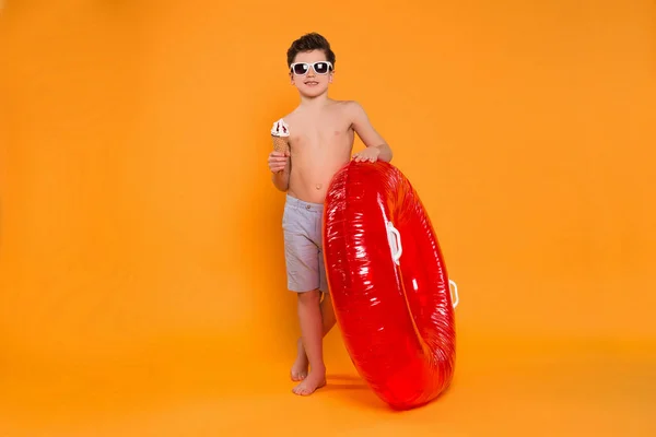 Der Sommer ist auf dem Weg! attraktiver junger Mann mit Brille, der mit dem Schwimmring zum Strand läuft und leckeres Eis isst. — Stockfoto