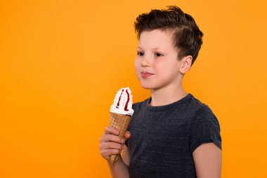 Zevk ile vakit geçirmek! Dondurma turuncu arka plan üzerinde kameraya poz külahı ile çok mutlu küçük çocuk portresi kadar yakın.
