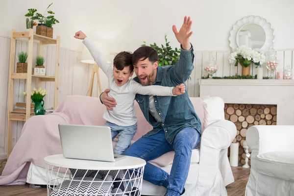 Seul le père peut enseigner le jeu et comment y jouer correctement ! Père très excité et heureux avec son fils regardant le football sur l'ordinateur portable, assis sur le canapé . — Photo