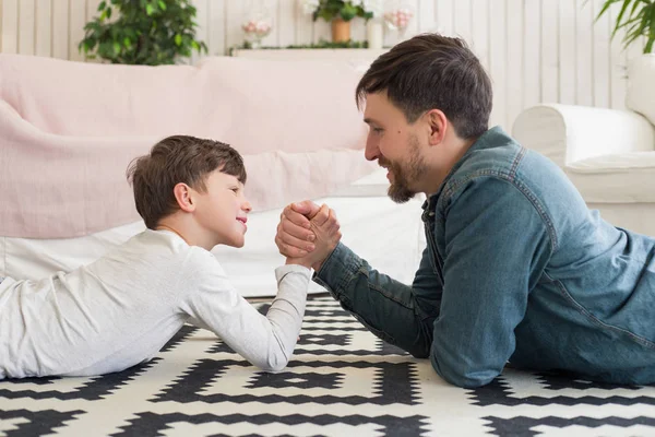 Père sait mieux que quiconque ! Portrait latéral du parent très gentil jouant avec son drôle de fils dans la lutte au bras de fer, tout en étant couché sur le sol . — Photo