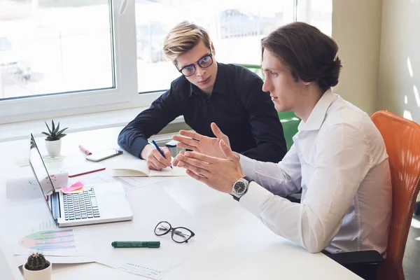 Your work is the purpose of your life! Freelancers using advanced technologies and printed diagrams, while speaking about their project beside the table.