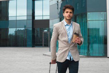 Bir iş ilgili olmak zorunda! Açık havada havaalanında Bagaj ile yürüme ve içme kahve-to-go genç harika iş adamı.