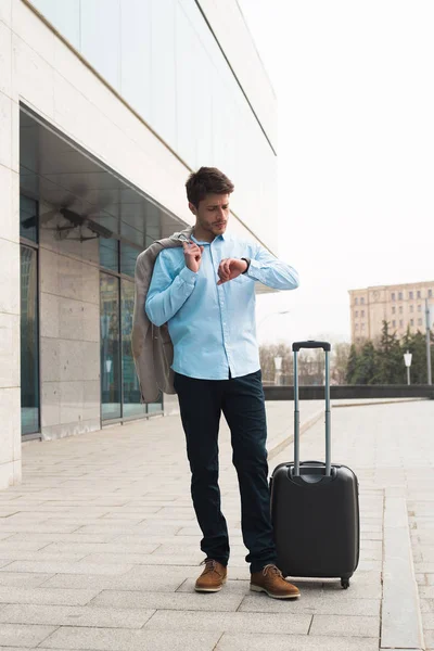 Tiempo para un largo viaje de negocios! Joven lleno de energía y entusiasmo hombre de negocios de pie en el aeropuerto y comprobar la hora de su vuelo . — Foto de Stock