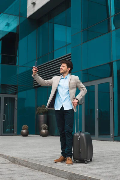 Passionné par son travail ! Photo pleine longueur du bel homme d'affaires souriant ayant du temps libre et faisant des selfies, en attendant son vol à l'aéroport . — Photo