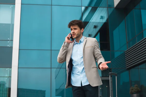 Conversaciones telefónicas! Hombre de negocios guapo serio hablando en voz alta en el teléfono inteligente, mientras espera su salida cerca del aeropuerto . — Foto de Stock