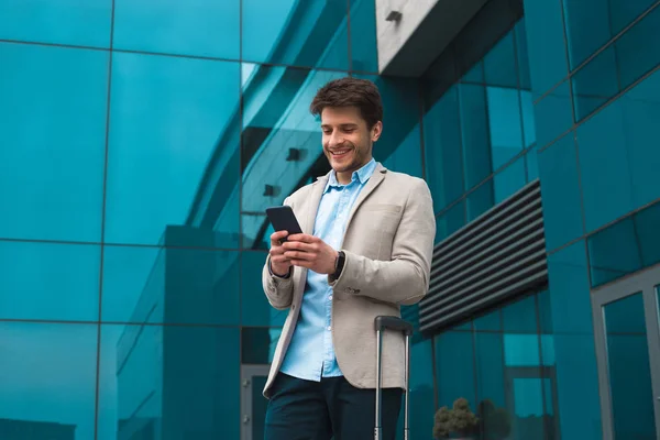 ¡Logrando su éxito! Sonriente joven guapo en viaje de negocios mensajes de texto de negocios desde su teléfono celular para informar a sus colegas de haber alcanzado su objetivo . — Foto de Stock