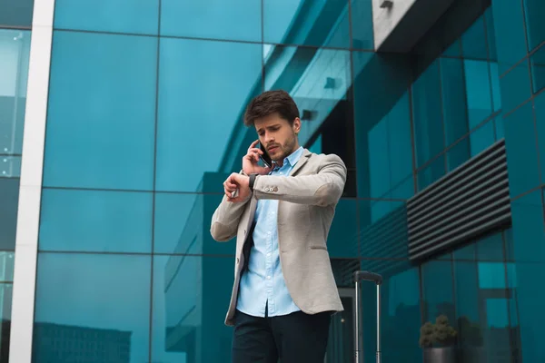 ¡Habla de negocios! Joven serio lleno de energía hombre de negocios de pie cerca del aeropuerto y comprobar la hora de su avión . — Foto de Stock