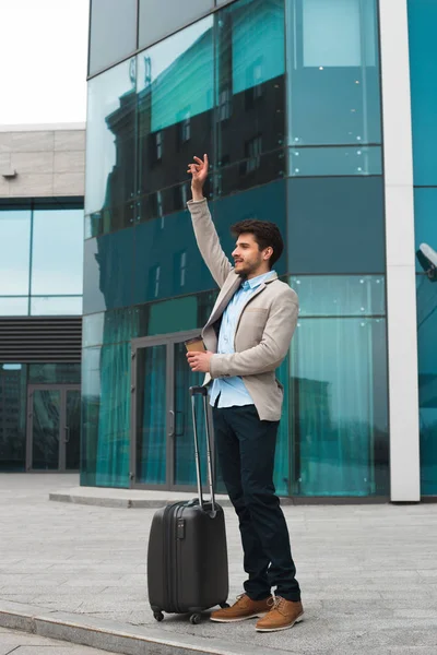 Réussir ! Souriant beau jeune homme étant venu après un voyage d'affaires, buvant son café et agitant le taxi afin d'obtenir son bureau . — Photo