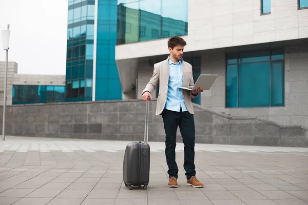 Travail multi-tâches ! Portrait complet du beau jeune homme d'affaires avec son ordinateur portable debout à l'aéroport, en attendant son départ . — Photo