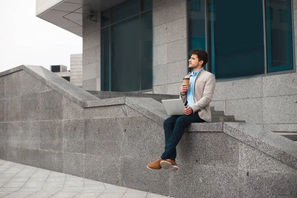 ¡Hora de descansar! Soñando joven casual inteligente sentado al aire libre y bebiendo café para llevar, mientras está en el aeropuerto y esperando su vuelo . — Foto de Stock