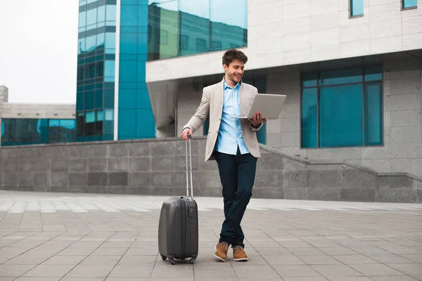 Vamos em frente! Sorrindo empresário incrível segurando um laptop e de pé com bagagem no aeroporto, enquanto espera por seu voo no exterior . — Fotografia de Stock