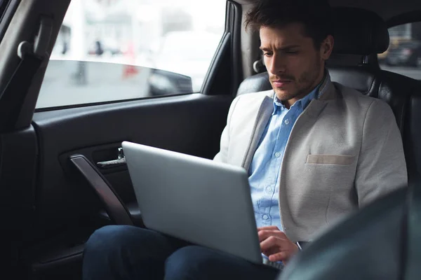 ¡Gana dinero fácilmente! Inteligente impresionante reconocido hombre mientras está sentado en el coche, utilizando su computadora inalámbrica y hacer su propio negocio . — Foto de Stock