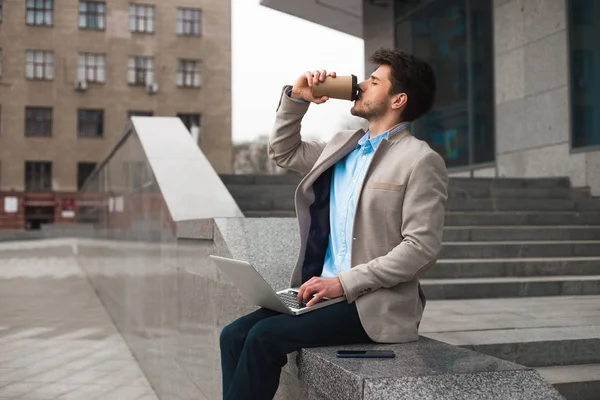 ¡Todo el mundo necesita relajarse! Guapo joven empresario serio bebiendo café para ir y sentado cerca del aeropuerto, mientras que tiene un tiempo libre . — Foto de Stock