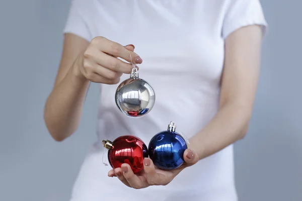 Dívka v bílém tričku drží vánoční hračka tři koule. Stříbrná, červená, modrá — Stock fotografie