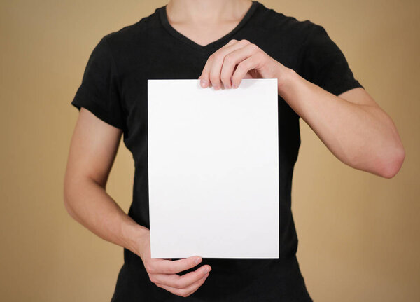 Man in black t shirt holding blank white A4 paper. Leaflet prese