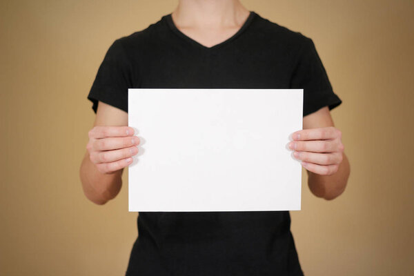 Man in black t shirt holding blank white A4 paper. Leaflet prese