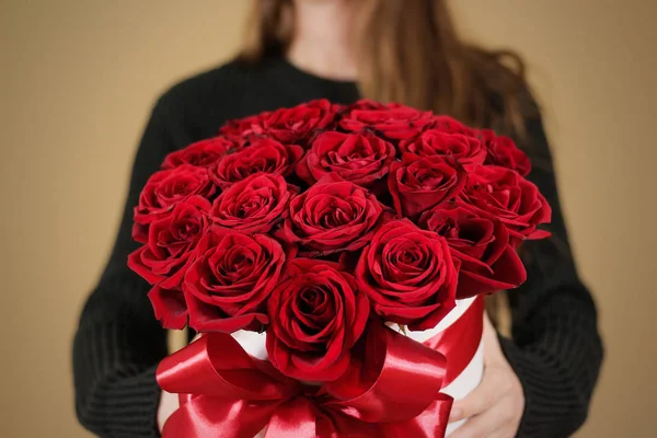 Kız 21 kırmızı gül buketi el zengin hediye tutarak siyah ceketli. Kompozisyon bir beyaz şapka çiçek dolu. Geniş kırmızı kurdele ve yay ile bağlı.