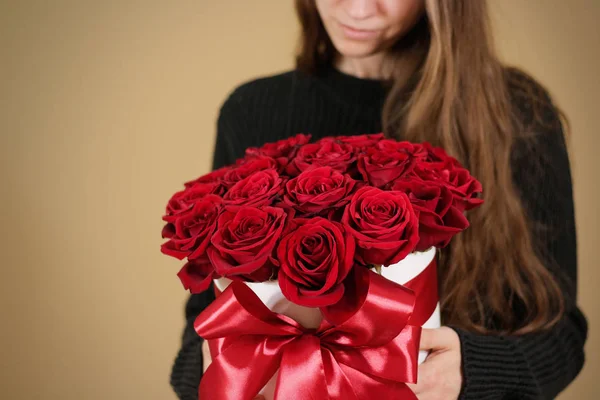 Mädchen in schwarzer Jacke mit einem reichhaltigen Blumenstrauß aus 21 roten Rosen in der Hand. Komposition von Blumen in einer weißen Hutschachtel. gebunden mit breitem rotem Band und Schleife. — Stockfoto
