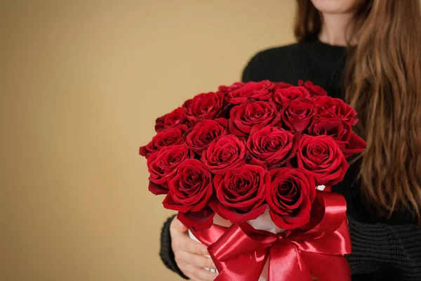 穿黑夹克抱着牵手丰富礼品花束 21 红玫瑰的女孩。在白色的帽盒花的组成。带着弓和宽红丝带绑. — 图库照片