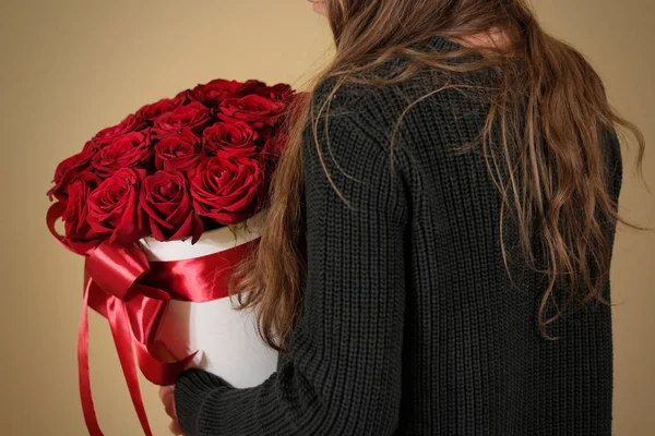 Kız 21 kırmızı gül buketi el zengin hediye tutarak siyah ceketli. Kompozisyon bir beyaz şapka çiçek dolu. Geniş kırmızı kurdele ve yay ile bağlı.