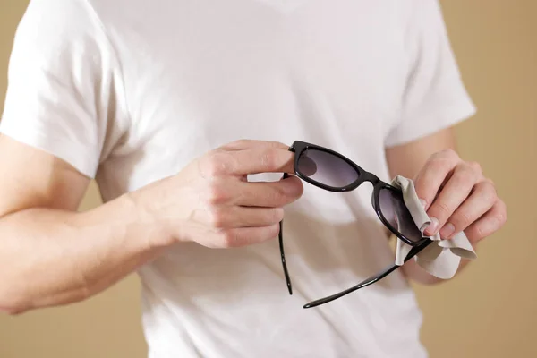 Hombre en camiseta blanca limpiando a mano lentes de sol negras con i —  Fotos de Stock