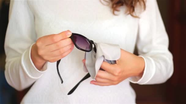 Women hand cleaning black sunglasses lens with blur brown background. — Stock Video