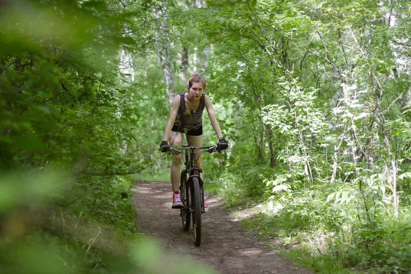 Hermosa chica está montando una bicicleta de montaña a través del bosque en un — Foto de Stock
