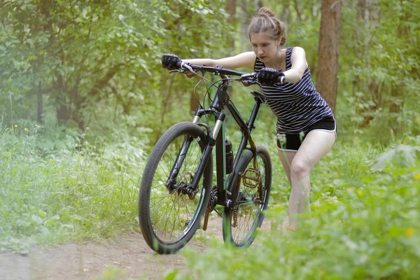 Vacker flicka rider en mountainbike genom skogen på en — Stockfoto