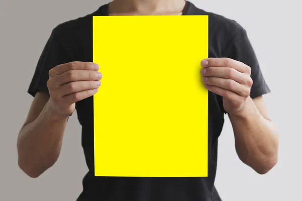 Homem de t-shirt preta segurando papel A4 amarelo em branco verticalmente. L — Fotografia de Stock