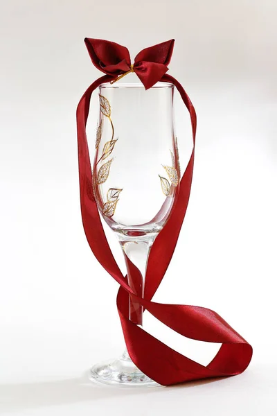 Empty glass goblet with a red ribbon with a bow. On a white back — Stock Photo, Image