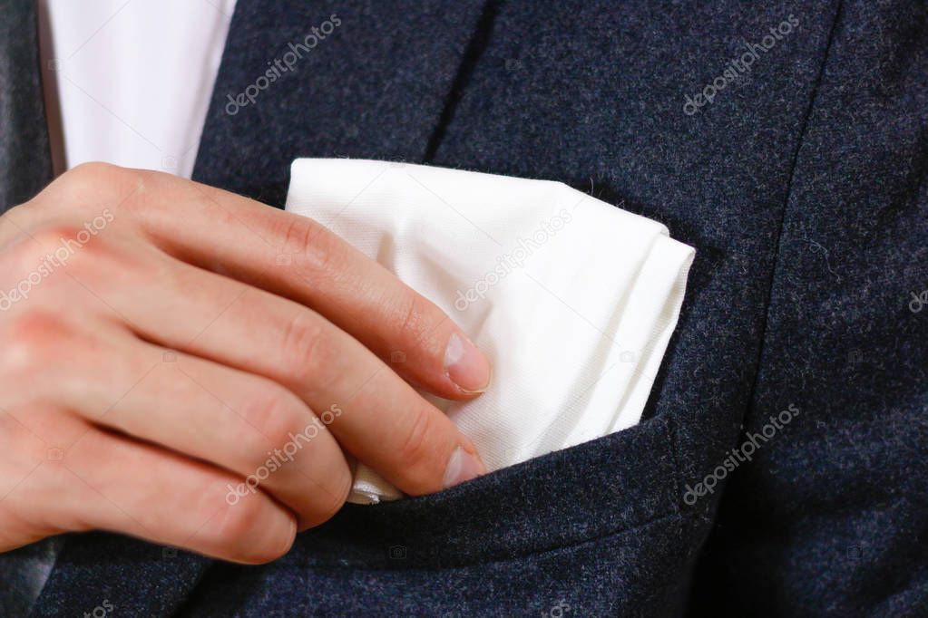 Close up hand puts a white handkerchief in the pocket of his bla