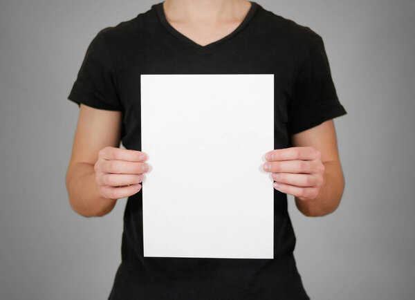Man in black t shirt holding blank white A4 paper. Leaflet prese