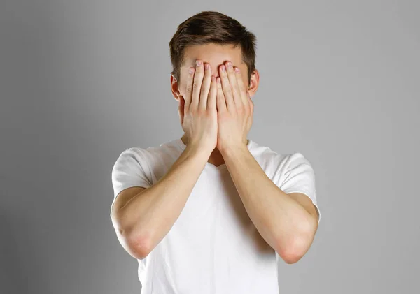 Man in white t-shirt covering his face with hands over gray back — Stock Photo, Image