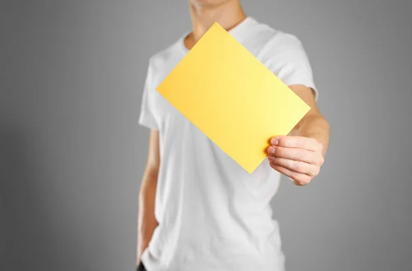 Um homem tem um papel amarelo na mão. Mostra um folheto em branco. Iso. — Fotografia de Stock