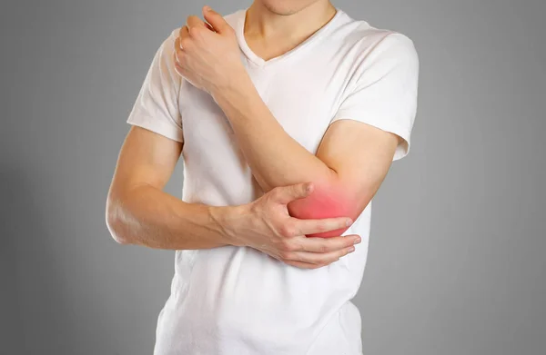 Un uomo tiene il gomito. Il dolore al braccio. Un punto dolente in rosso . — Foto Stock