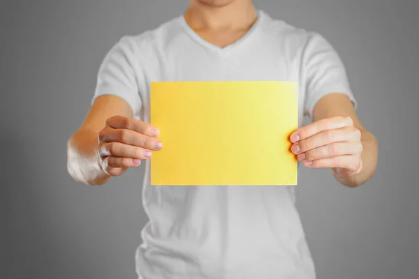 Um homem tem um papel amarelo na mão. Mostra um folheto em branco. Iso. — Fotografia de Stock