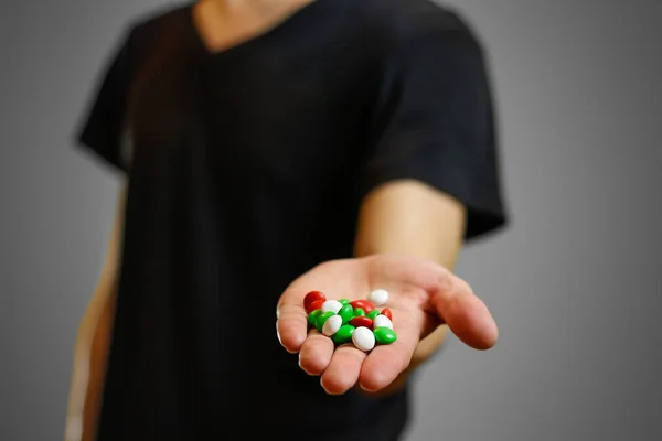 A man in a black t-shirt holding a colorful pill. Bright colored
