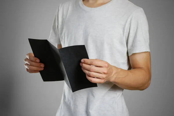 Ένας άντρας σε ένα γκρι t-shirt κρατώντας κενό σαφές μαύρο του φύλλου. — Φωτογραφία Αρχείου