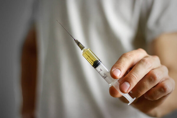 A young man holding a syringe with a needle with the drug. Close