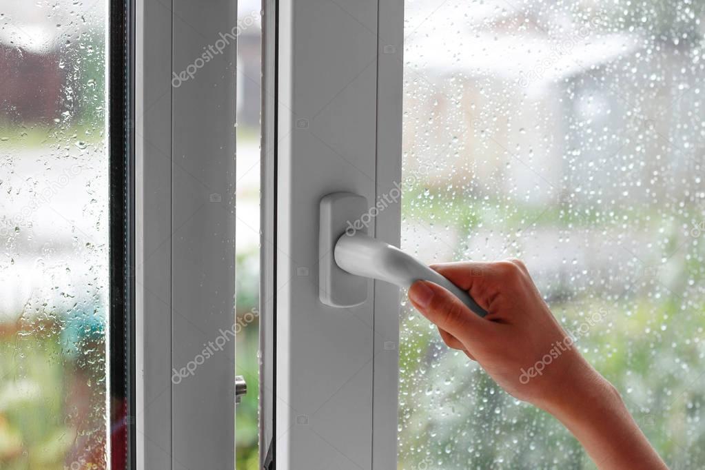 A female hand opens a window with water drops. Closes the window