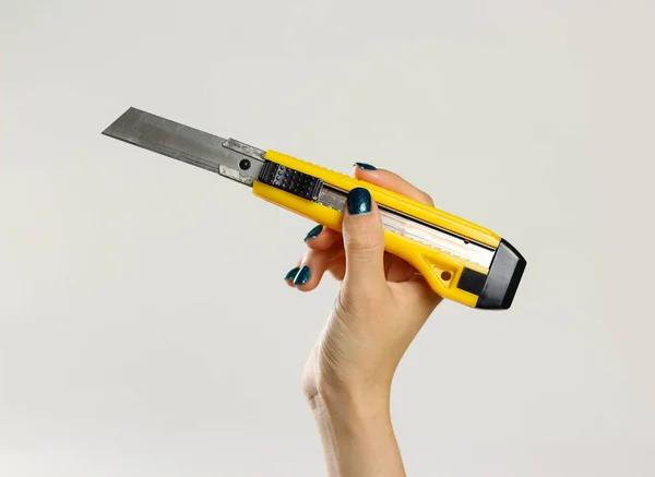 Female hands holding yellow sharp box cutter. Isolated on gray b — Stock Photo, Image