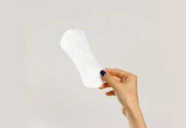 Beyaz bir hijyenik ped tutan eller. Gri arkasında izole