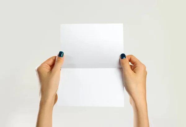 Des mains féminines tenant une feuille de papier blanche. Isolé sur ba gris — Photo