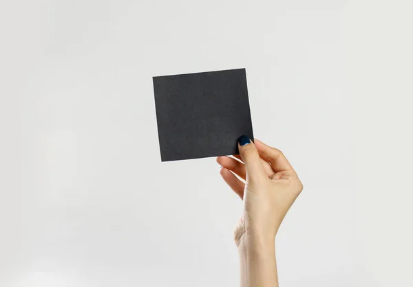 Manos femeninas sosteniendo una hoja negra de papel. Aislado en ba gris — Foto de Stock
