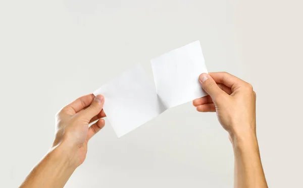 Αρσενικό χέρια rip ένα λευκό φύλλο χαρτί. Απομονωμένα σε γκρι λεμονάτα — Φωτογραφία Αρχείου